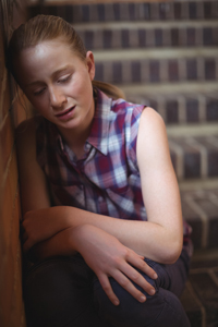 Unhappy secondary schoolgirl crying on a flight of stairs